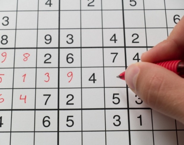 A hand holding a pen on a sudoku grid.